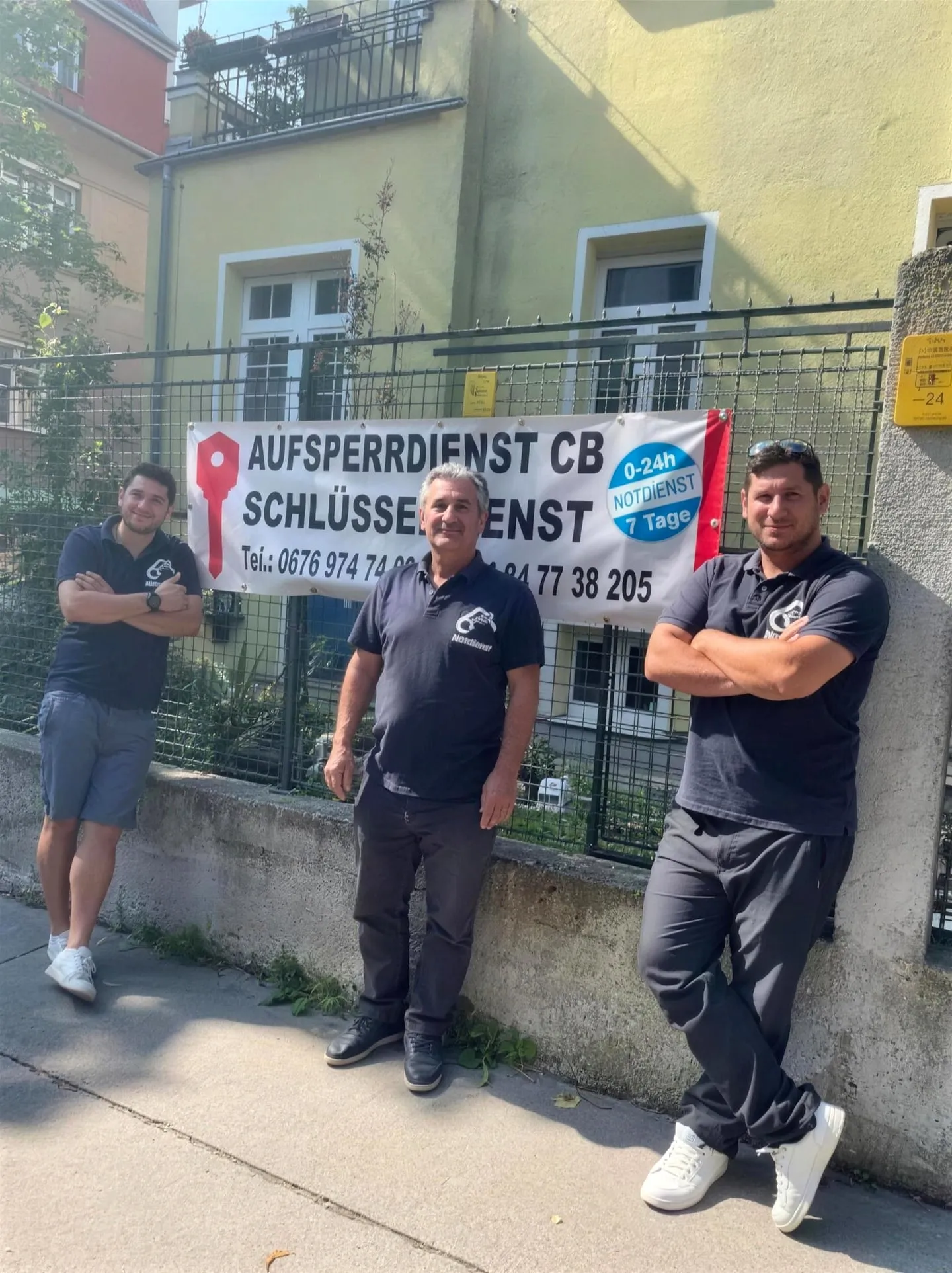 A father and his two sons in company polo shirts in front of the Aufsperrdienst CB banner in Vienna.