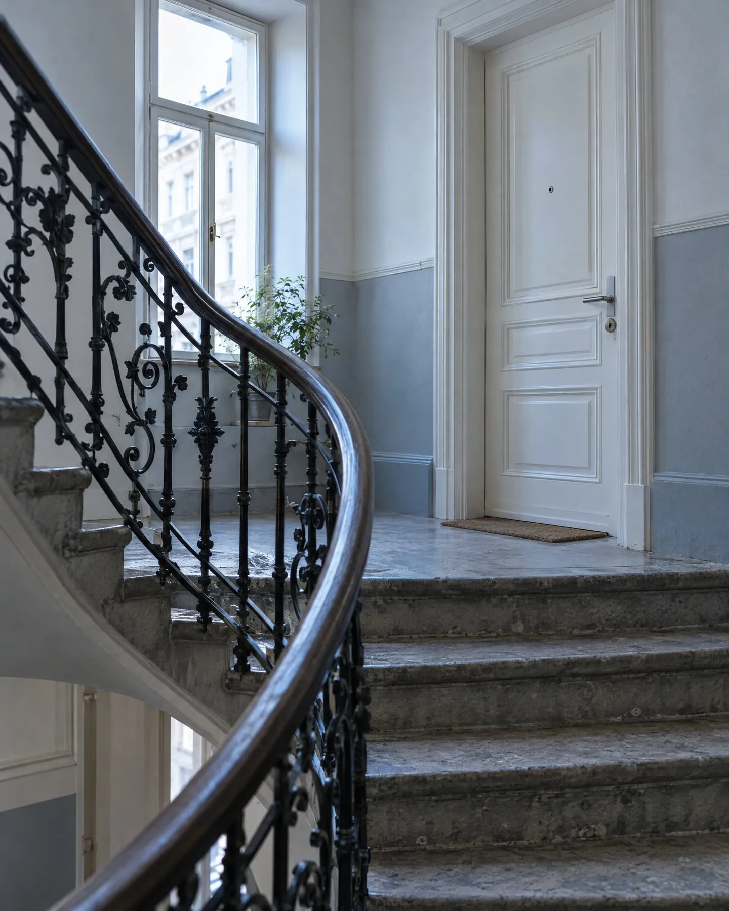 Stiegenhaus eines Wiener Altbaus mit schmiedeeisernem Geländer und weißer Wohnungstür.